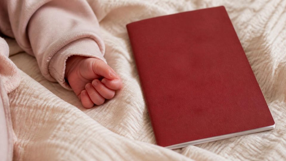 A baby's hand resting beside a passport on a cream blanket