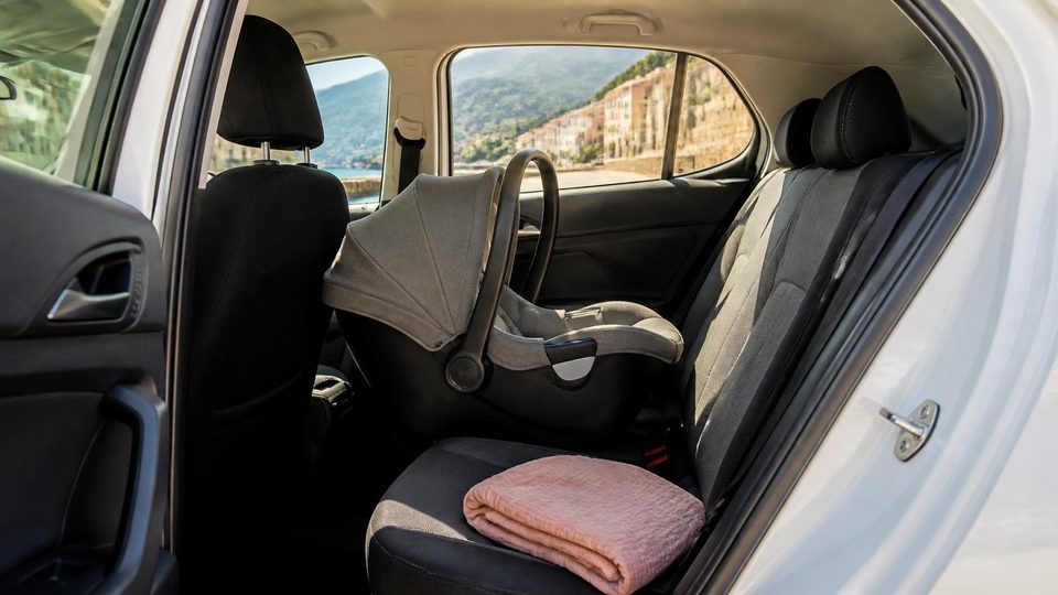 An infant car seat fitted in the back of a hire car on a coastal road