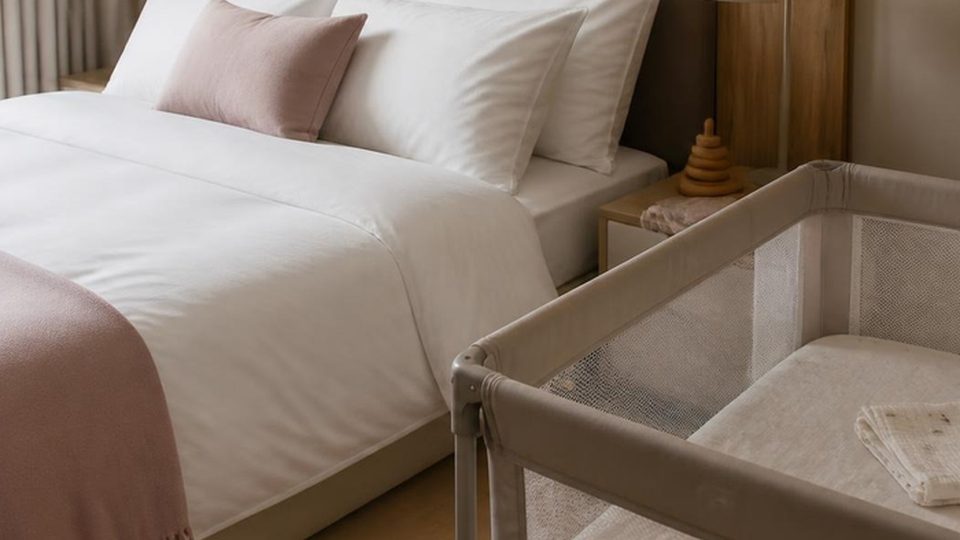 A travel cot beside a made-up hotel bed
